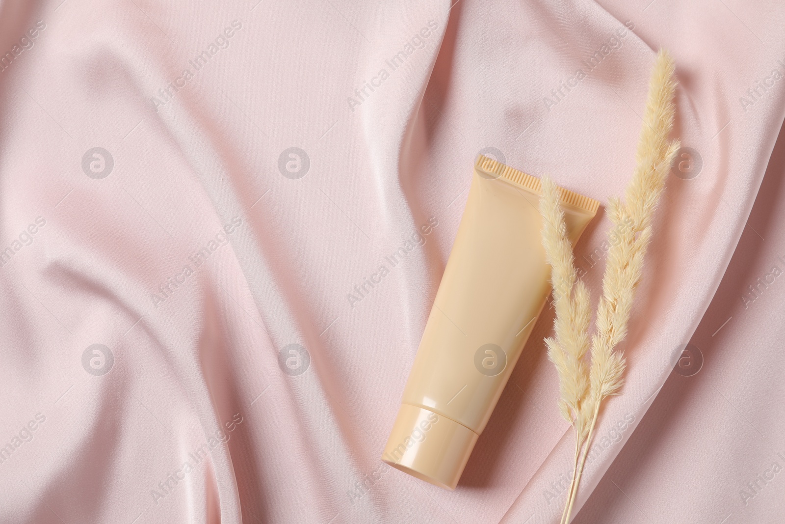 Photo of Tube of skin foundation and dried reeds on pink cloth, flat lay with space for text. Makeup product