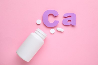 Photo of Pills, open bottle and calcium symbol made of purple letters on pink background, flat lay