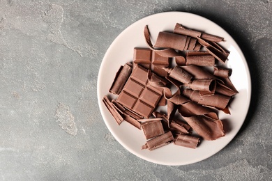 Photo of Plate with chocolate curls and pieces on grey background, top view. Space for text