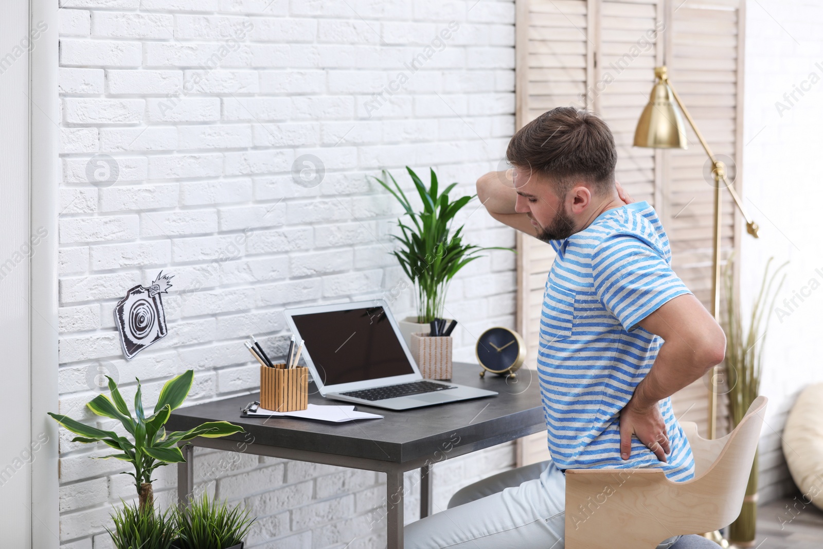 Photo of Young man suffering from back pain in office