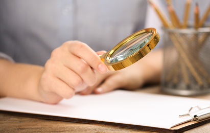 Photo of Woman using magnifying glass at table, closeup