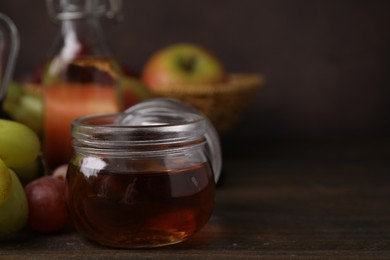 Photo of Vinegar in glass jar and grapes on wooden table, space for text