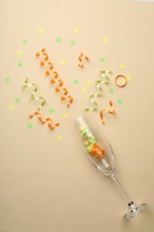Photo of Glass and shiny confetti on beige background, flat lay