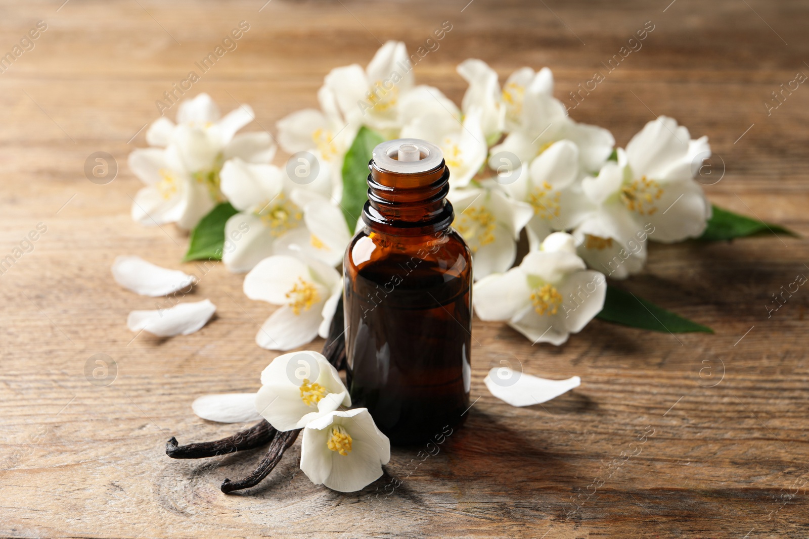 Photo of Jasmine essential oil and fresh flowers on wooden table