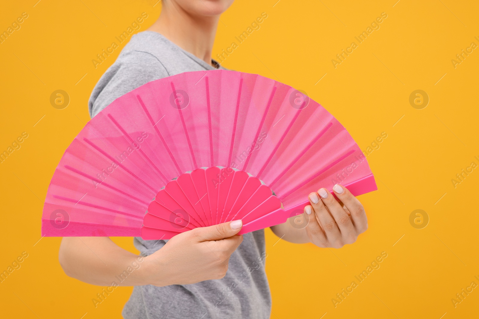 Photo of Woman holding hand fan on orange background, closeup