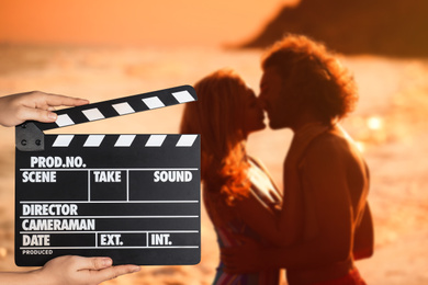 Assistant holding clapperboard and people kissing on beach at sunset, closeup. Cinema production 