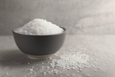 Photo of Natural salt in bowl on grey textured table, space for text