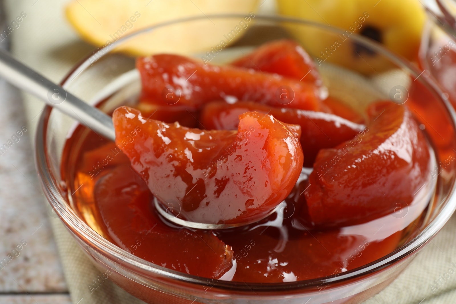 Photo of Taking tasty homemade quince jam from bowl at table, closeup