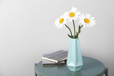 Photo of Beautiful tender chamomile flowers in vase and notebooks on table against light background, space for text