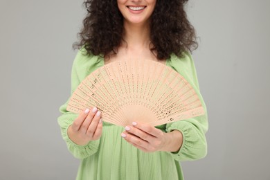 Woman holding hand fan on light grey background, closeup