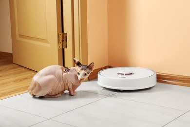 Photo of Robotic vacuum cleaner and cute Sphynx cat on floor indoors