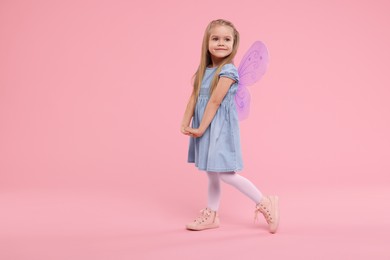Photo of Cute little girl in fairy costume with violet wings on pink background, space for text