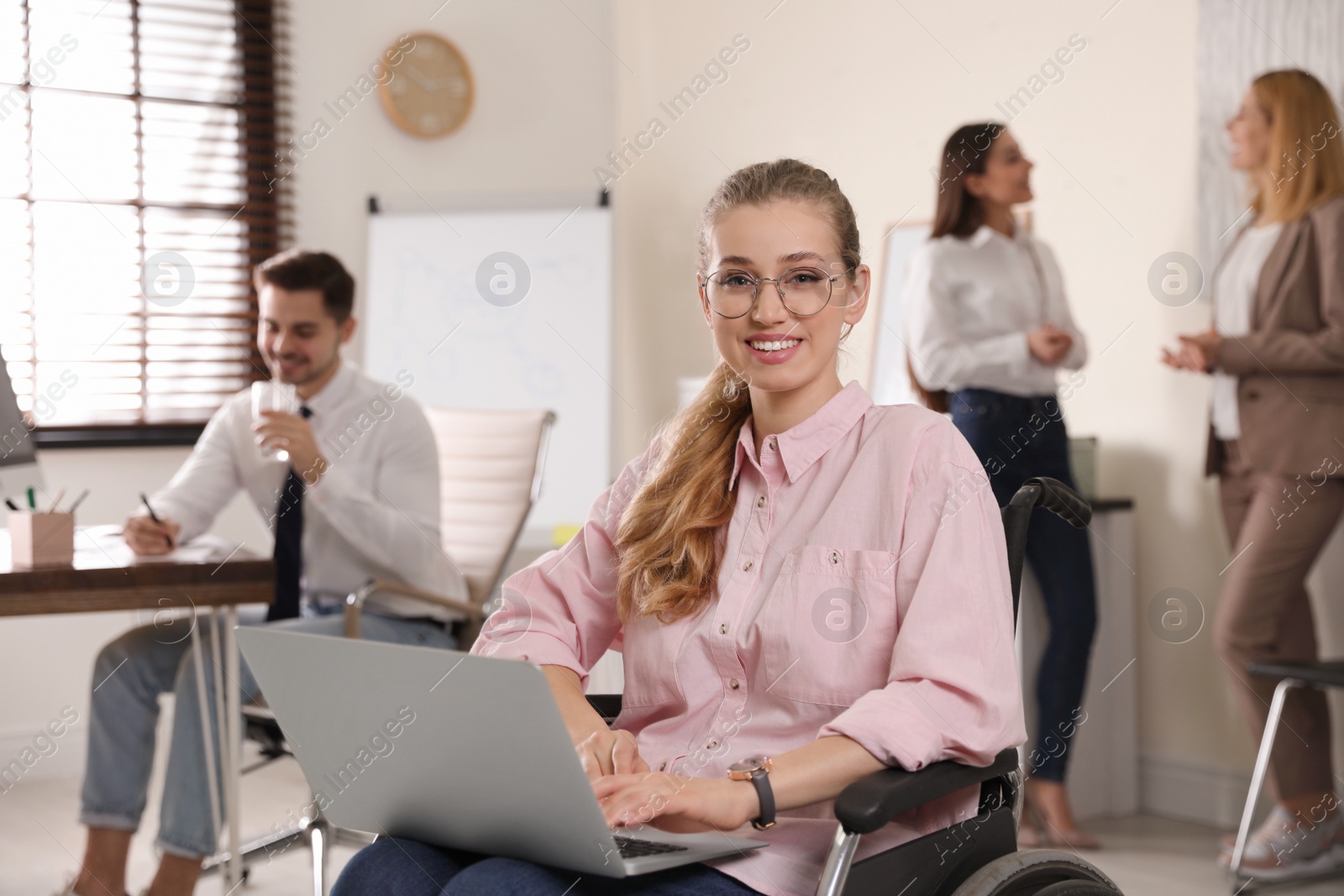 Photo of Portrait of woman in wheelchair with laptop and her colleagues at workplace