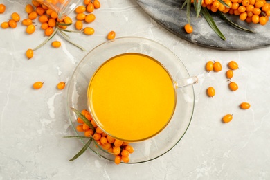 Photo of Delicious sea buckthorn tea and fresh berries on light grey table, flat lay