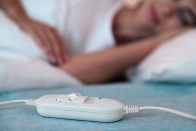 Photo of Young woman sleeping in bed with electric heating pad, focus on cable
