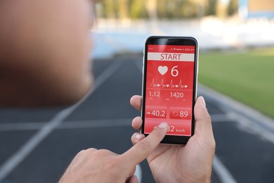 Man using fitness app on smartphone at stadium, closeup