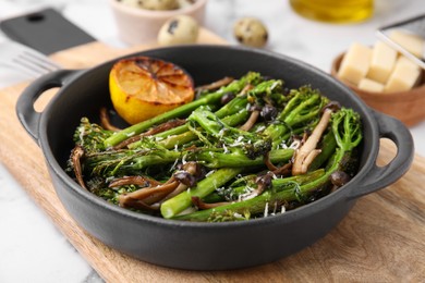 Photo of Tasty cooked broccolini, mushrooms and lemon on wooden board, closeup