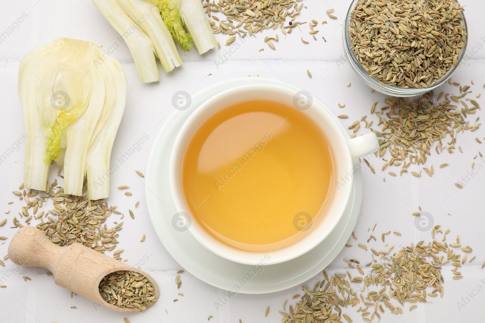 Photo of Fennel tea in cup, seeds and fresh vegetable on white tiled table, flat lay