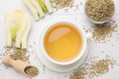 Fennel tea in cup, seeds and fresh vegetable on white tiled table, flat lay