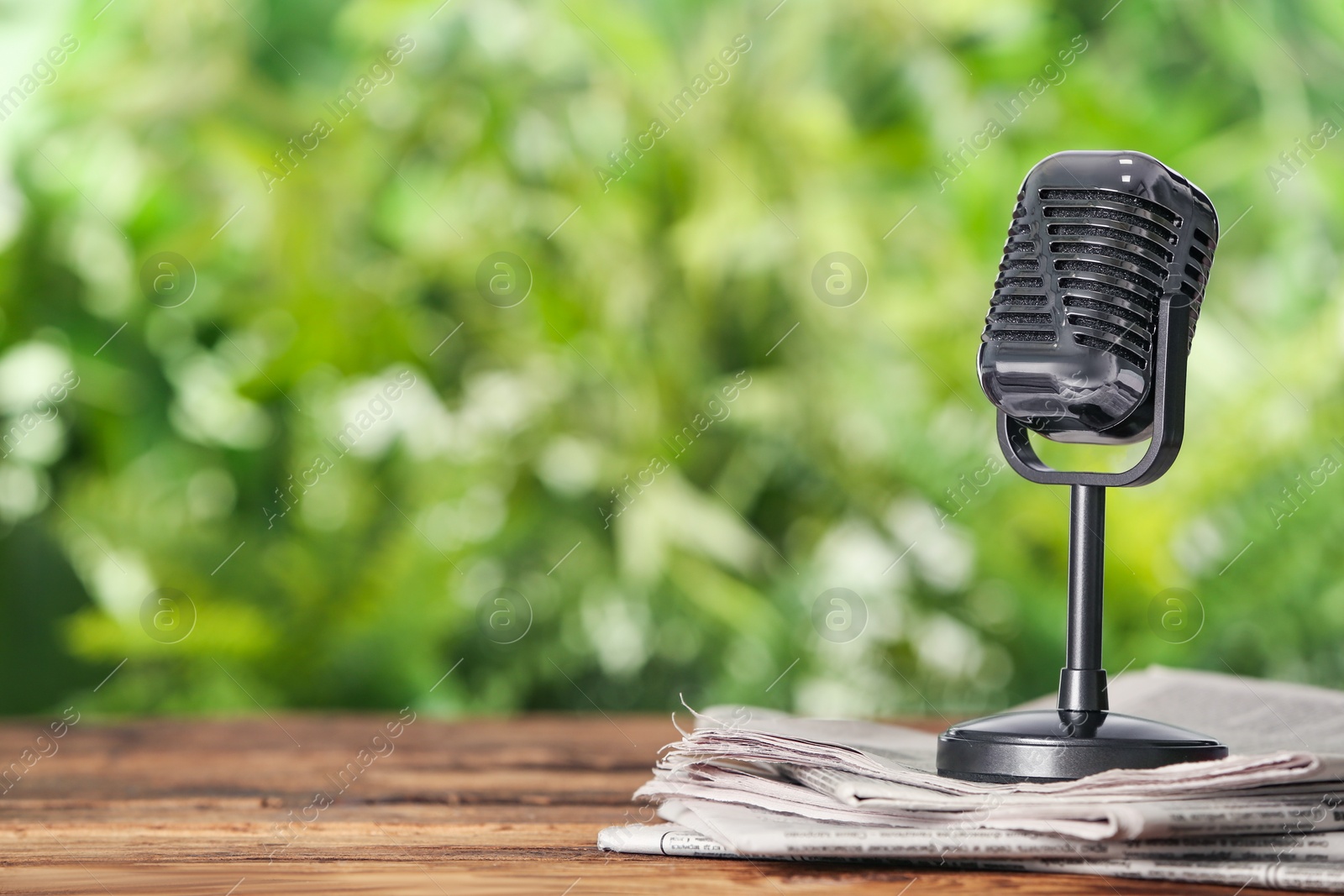 Photo of Newspapers and vintage microphone on wooden table against blurred green background, space for text. Journalist's work