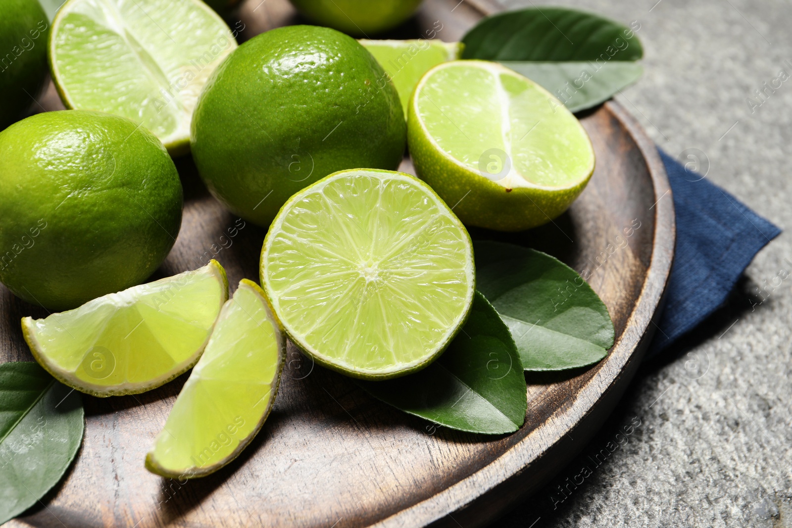 Photo of Fresh ripe limes and leaves on grey table, closeup