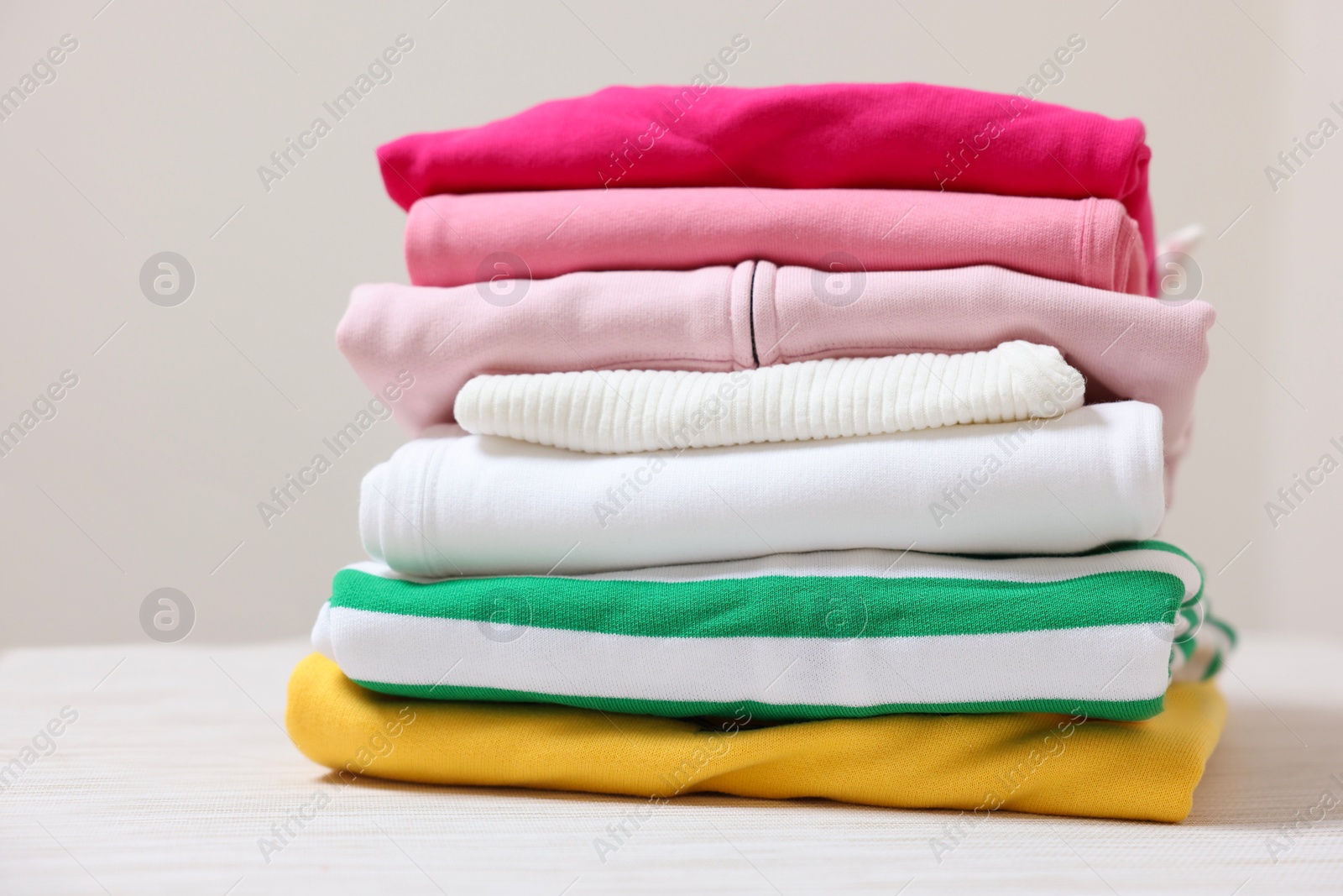 Stack of folded clothes on table against beige background Photo of Stack of folded clothes on table against beige background