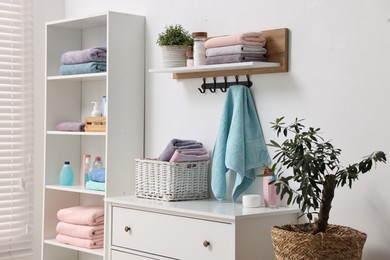 Photo of Fresh towels, laundry basket and toiletries on chest of drawers indoors