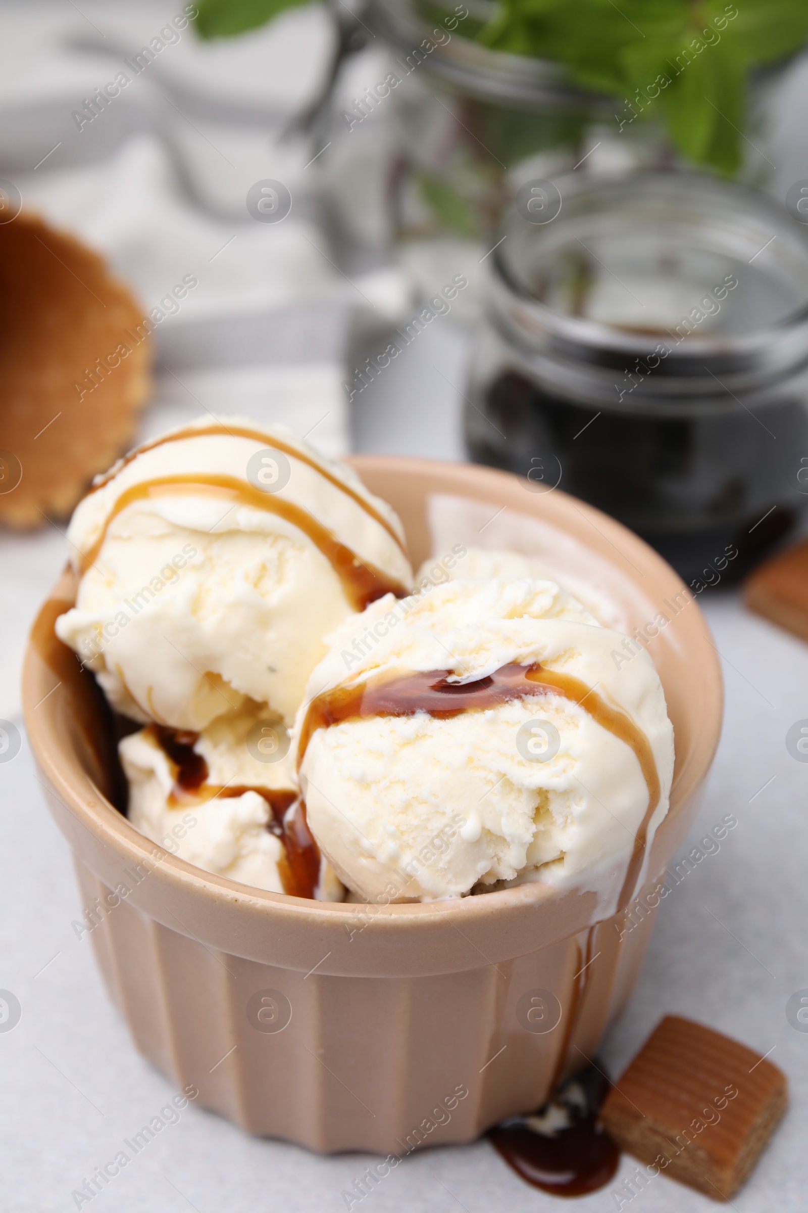 Photo of Scoops of ice cream with caramel sauce and candies on light grey table, closeup