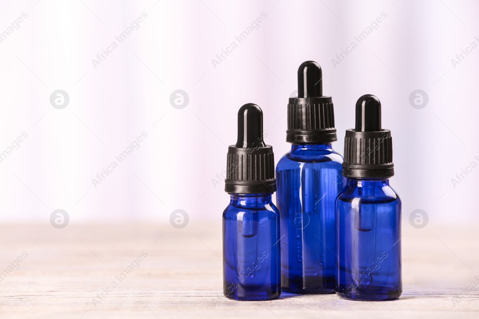 Photo of Bottles of essential oils on table against light background, space for text. Cosmetic products