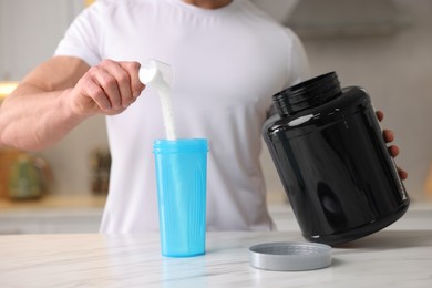 Photo of Young man making protein shake at white marble table in kitchen, closeup
