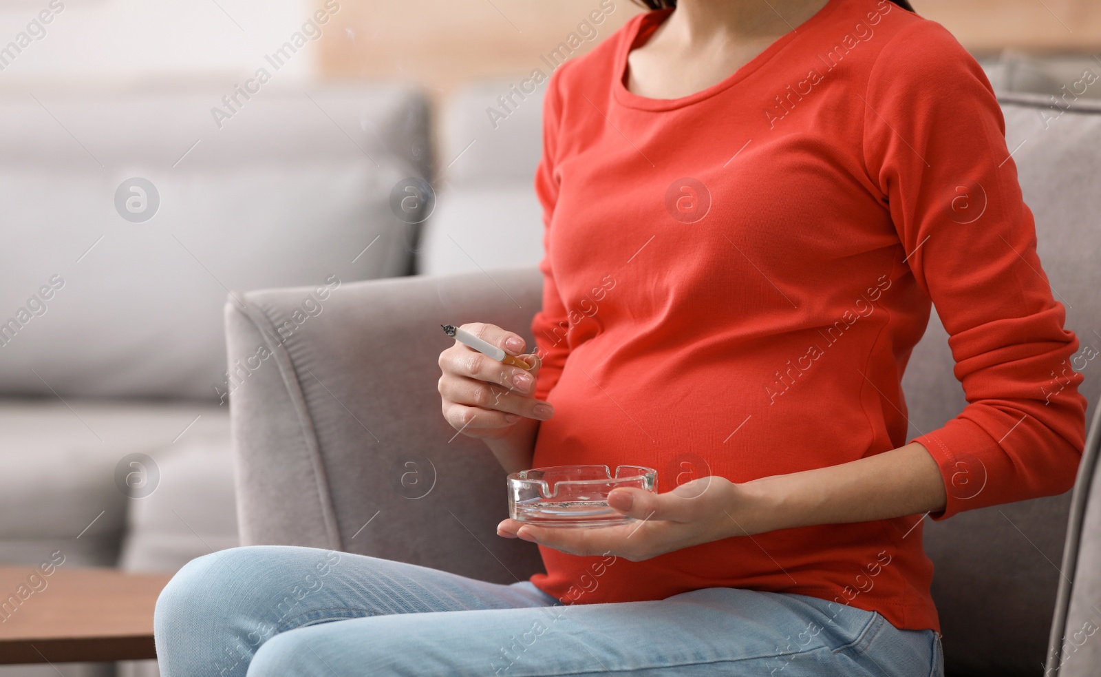 Photo of Young pregnant woman smoking cigarette at home, closeup. Space for text
