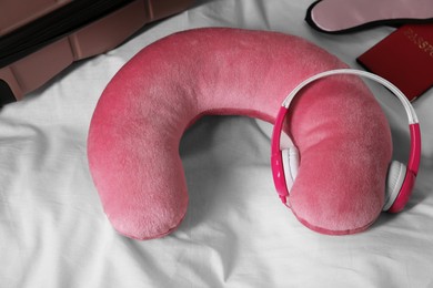 Photo of Pink travel pillow with headphones, suitcase, passport and sleep mask on bed