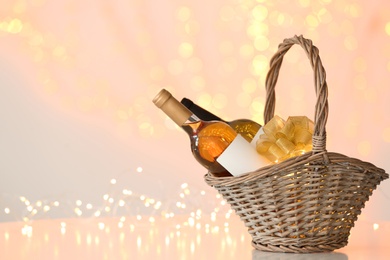 Photo of Wicker basket with bottles of wine against blurred lights. Space for text