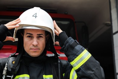 Photo of Firefighter in uniform wearing helmet near fire truck at station