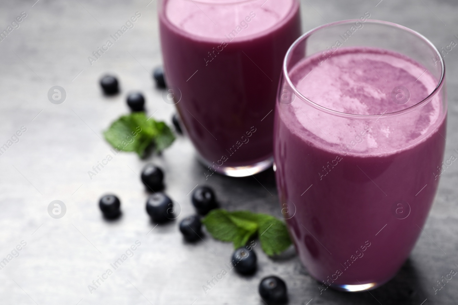 Photo of Tasty acai drink in glasses and berries on grey table, closeup. Space for text