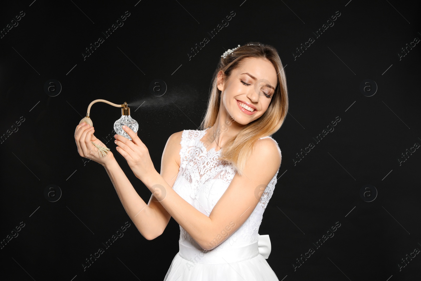 Photo of Beautiful young bride applying perfume against black background