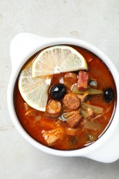 Meat solyanka soup with sausages, olives and vegetables in bowl on white textured table, top view