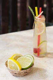 Refreshing tasty lemonade served in glass bottle and citrus fruits on beige table