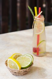 Photo of Refreshing tasty lemonade served in glass bottle and citrus fruits on beige table