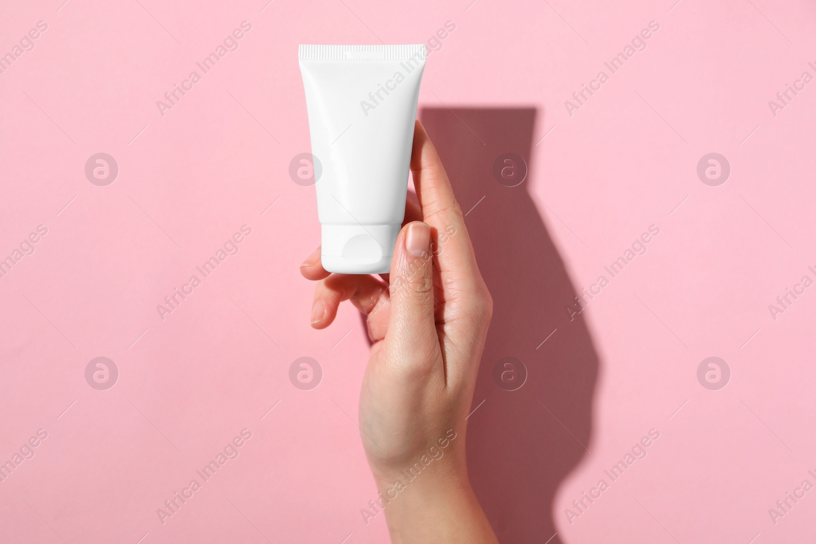 Photo of Woman with tube of hand cream on pink background, top view