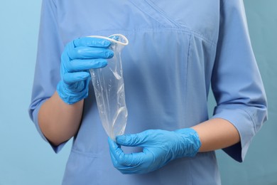 Doctor with unrolled female condom on light blue background, closeup. Safe sex