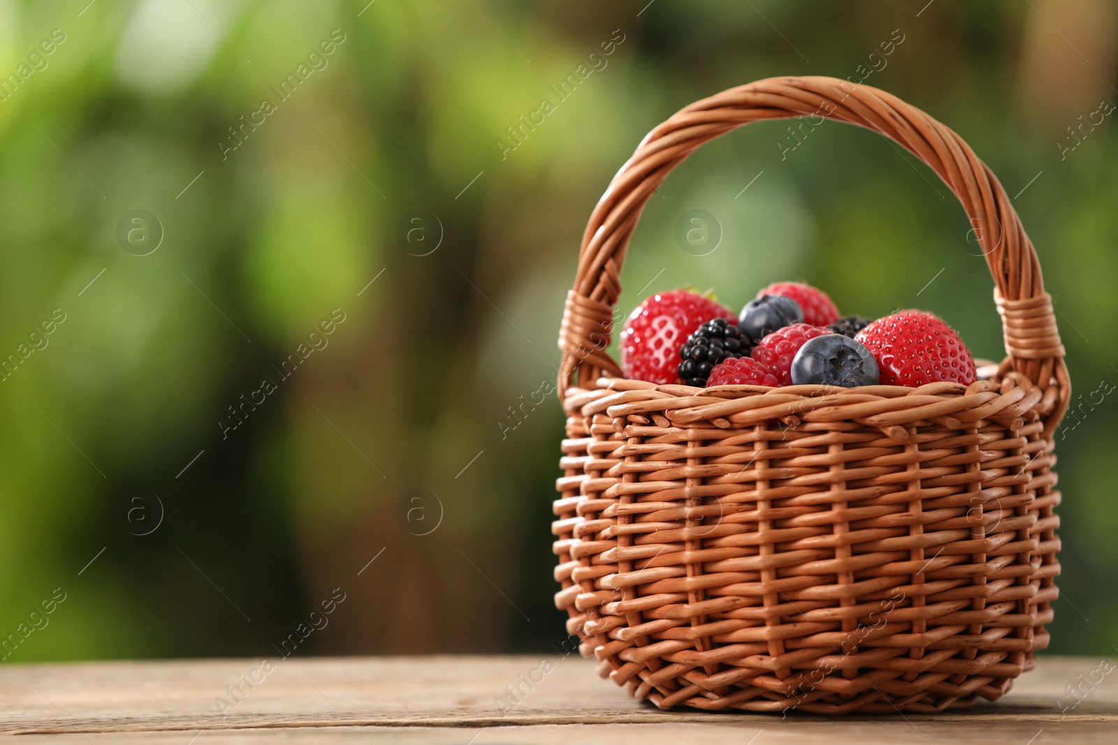 Wicker basket with different fresh ripe berries on wooden table outdoors, space for text Photo of Wicker basket with different fresh ripe berries on wooden table outdoors, space for text