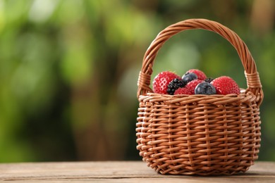 Photo of Wicker basket with different fresh ripe berries on wooden table outdoors, space for text