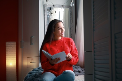 Photo of Young woman with book at home. Winter season