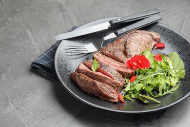 Photo of Delicious grilled beef meat served with greens on grey table