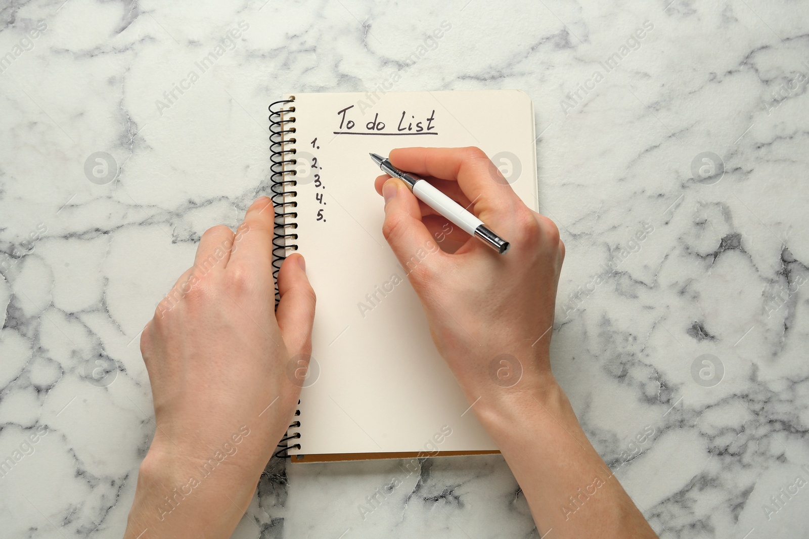 Photo of Woman filling To Do list in notepad at white marble table, top view