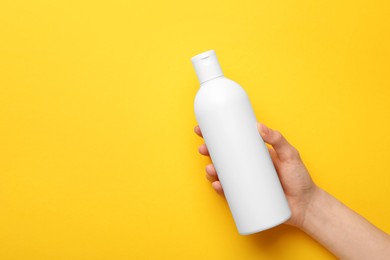 Photo of Woman holding shampoo bottle on yellow background, top view. Space for text