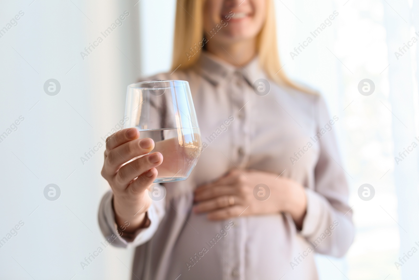 Photo of Young pregnant woman with glass of water indoors, closeup