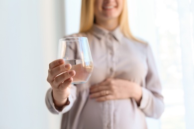 Young pregnant woman with glass of water indoors, closeup