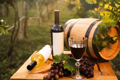 Composition with wine and ripe grapes on wooden table in vineyard